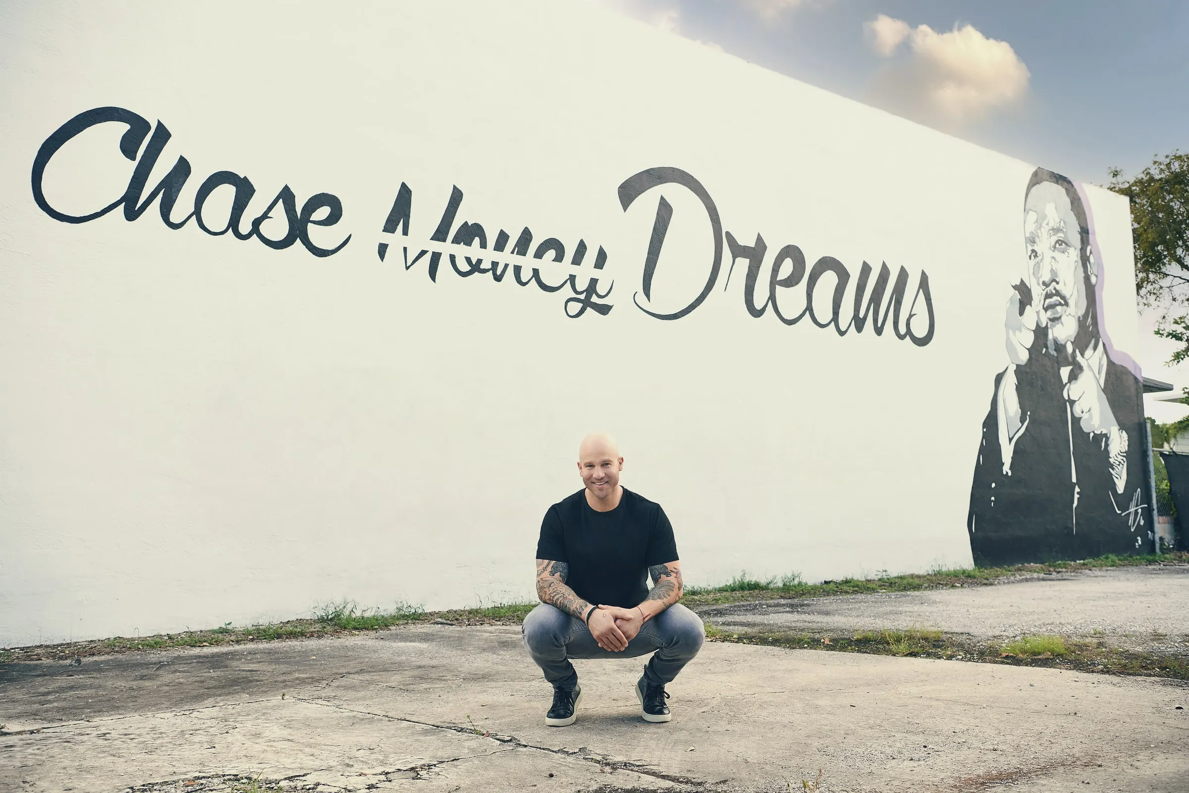 Jeff Halevy crouching in front of a mural that reads “Chase Money Dreams”, with “Money” crossed out